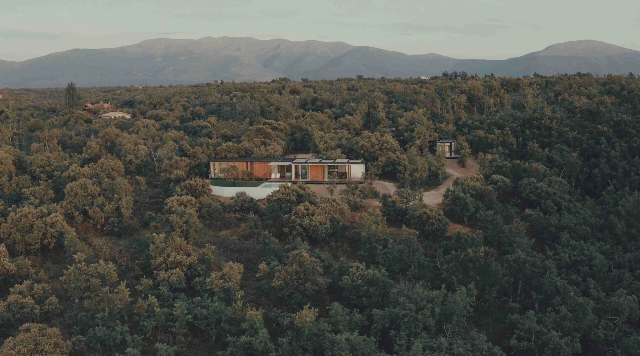 Aerial view of Tini Unit modular homes in a holm-oak landscape with mountains behind